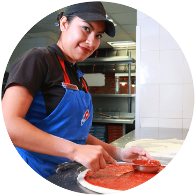 trabajadora de Domino's Pizza poniéndole salsa de tomate a la masa